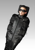 A person wearing a full-body black leather sleepsack with metal D-rings and zippers, covering from neck to feet, and equipped with eye masks and blindfolds.