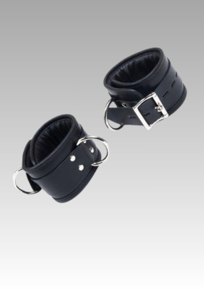 Two black leather cuffs with metal buckles on a gray background