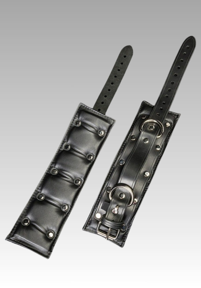 Black leather ankle restraints laid open with padded lining, D-rings and adjustment holes